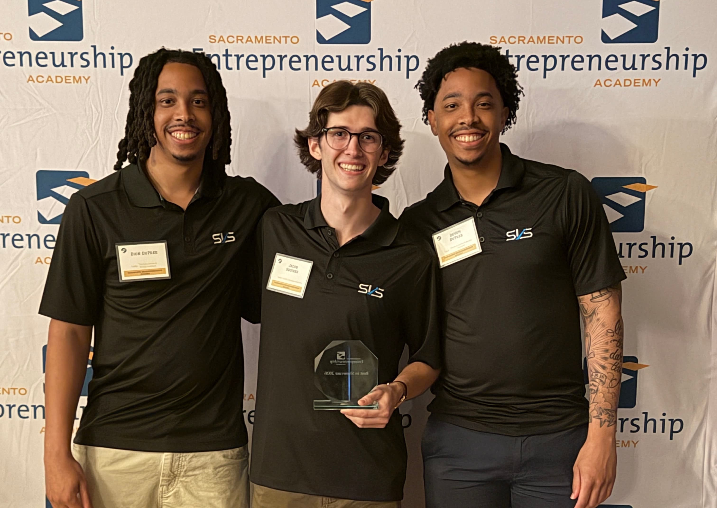 Left to right: Dion DuPree, Jacob Squires holding the Best in Showcase trophy, and DeVon DuPree at the 2026 Sacramento Entrepreneurship Academy showcase
